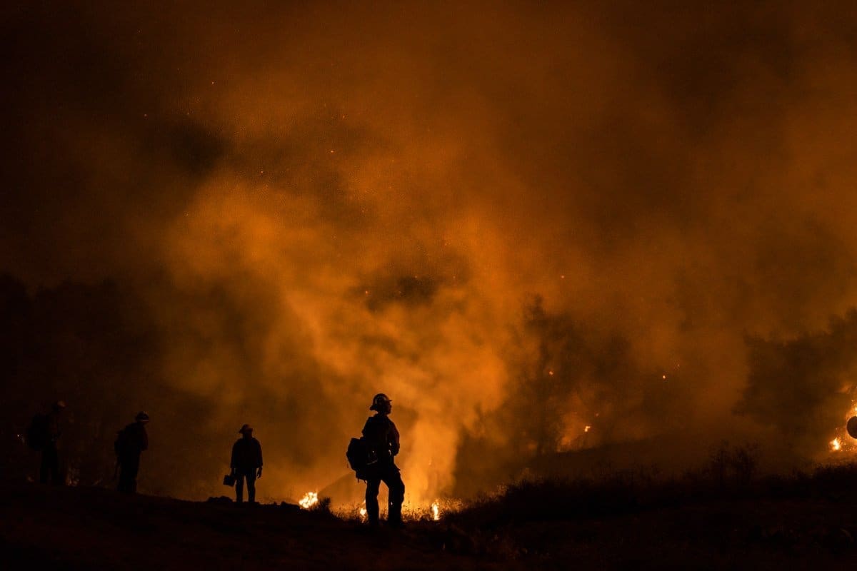 documentary photograph of firefighters standing in the red glow of smoke and flames created by the wildfires.