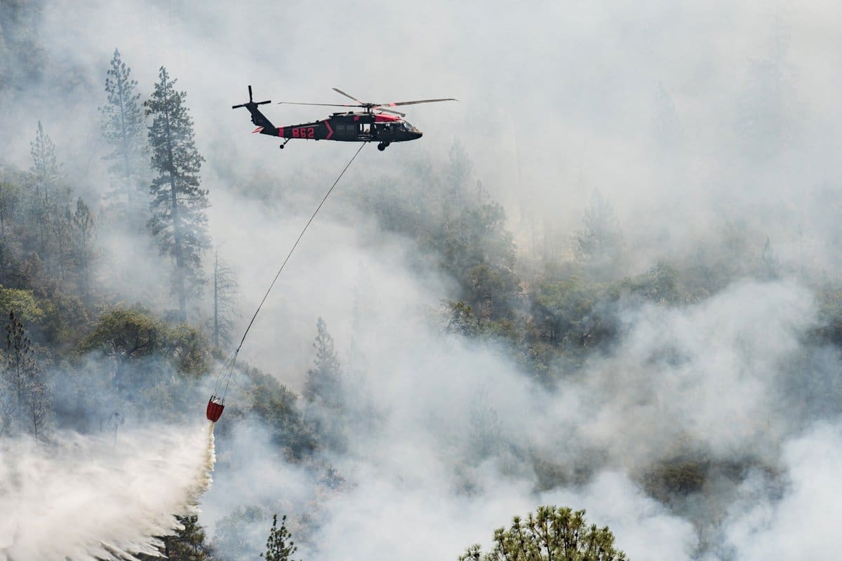 Documentary photography of a fire helicopter dousing flames and dropping water on the burnign forest below