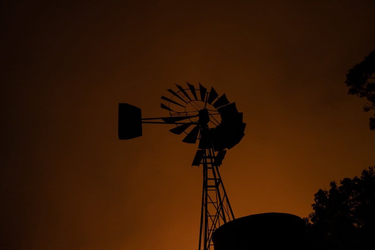 a windmill stands amidst an ominous smoky red sky created from wildfires in this documentary photo