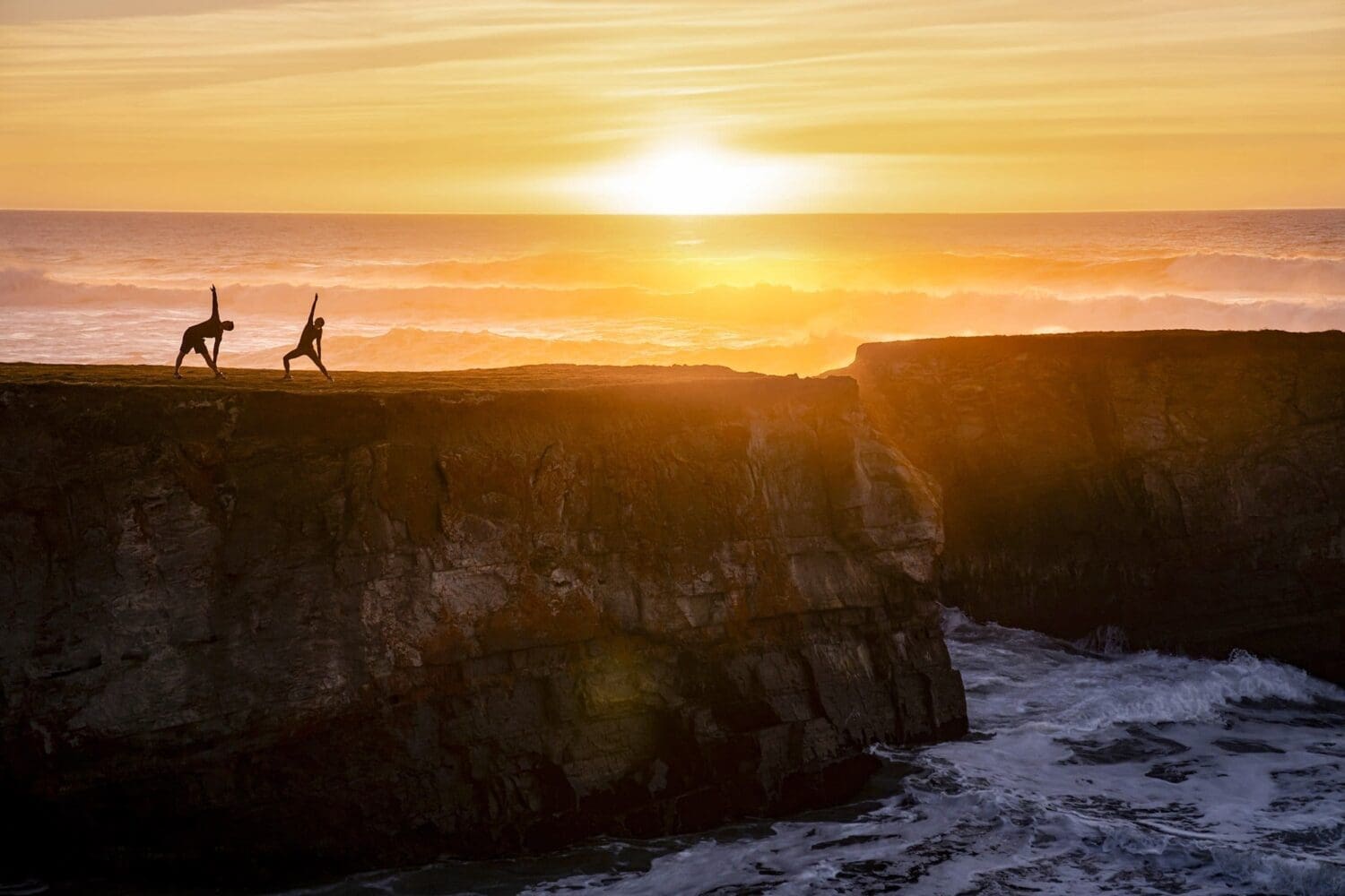 Outdoor lifestyle photograph of two people as they do yoga on the cliffs in California