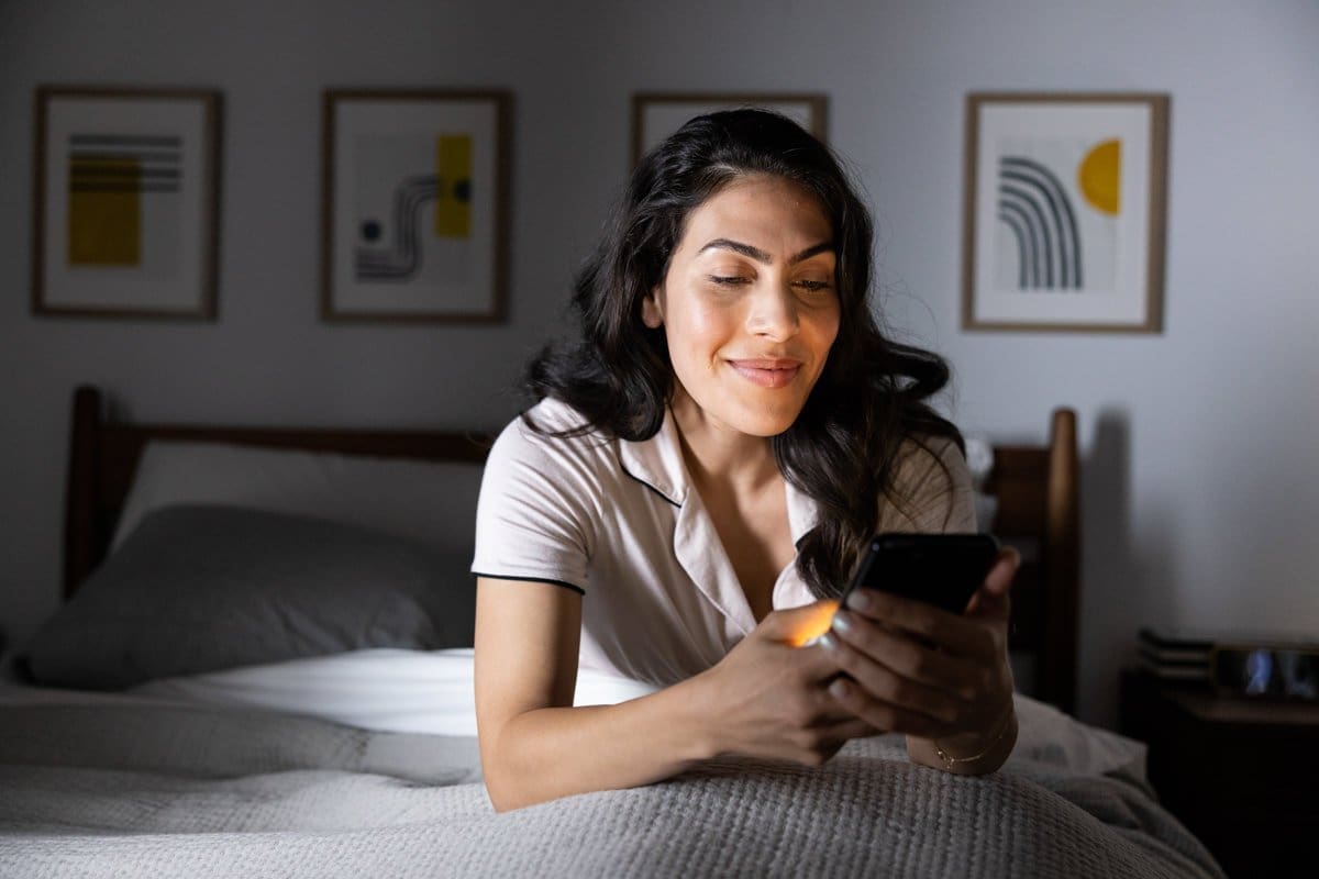 a woman laying in bed monitors her glucose levels from her phone in this commercial photograph