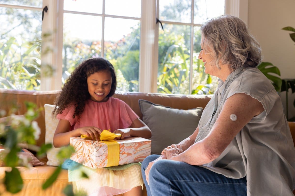 a woman wearing an Abbott CGM Sensor watches a young girl opening a present in this commercial photograph