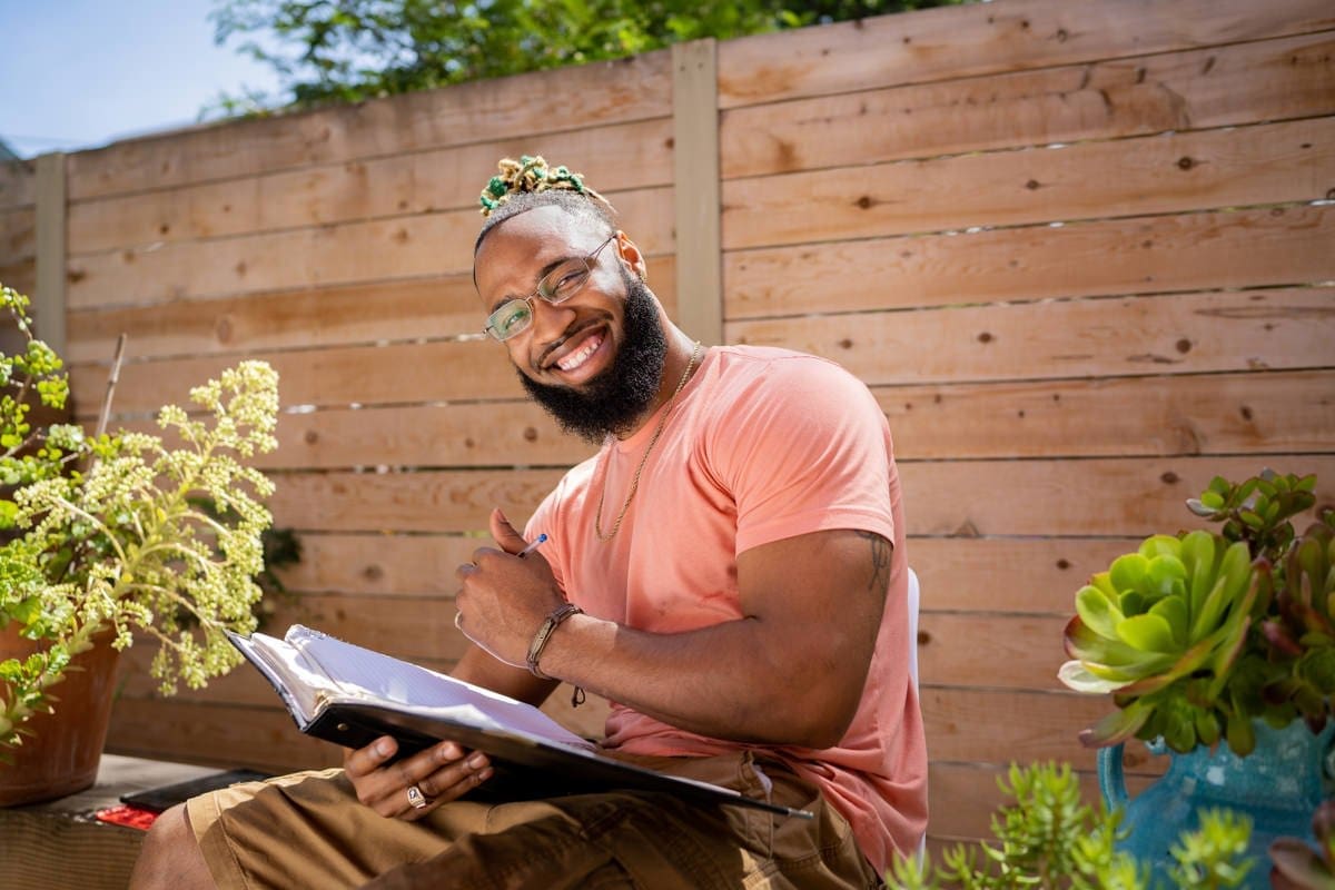 a student smiles and takes notes while seated outside in this commmercial photograph for CA Community Colleges