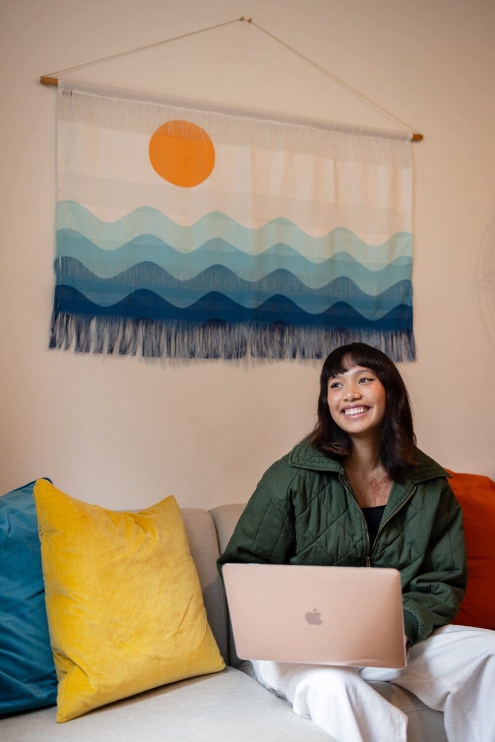 a smiling woman uses her laptop on a couch in this commercial photograph