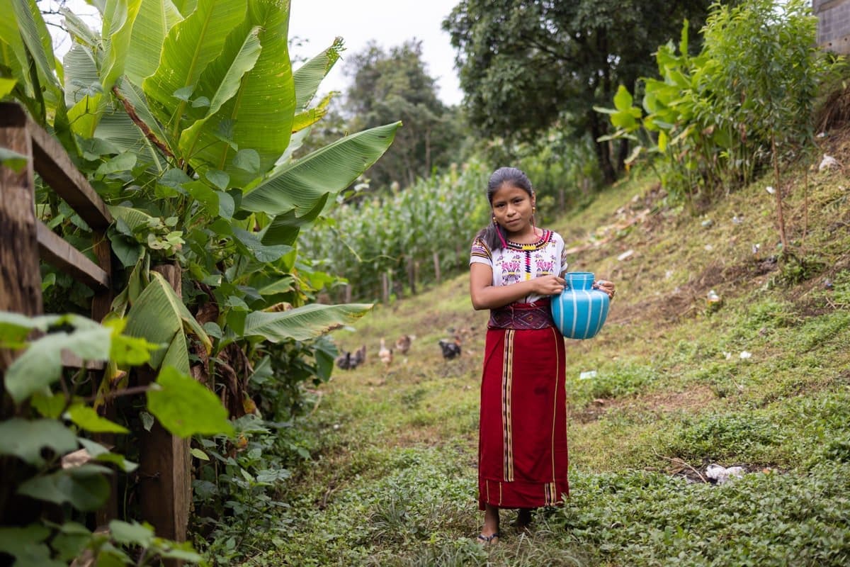 a young Guatemalan girl holds a pitcher of water as she prepares to carry it home